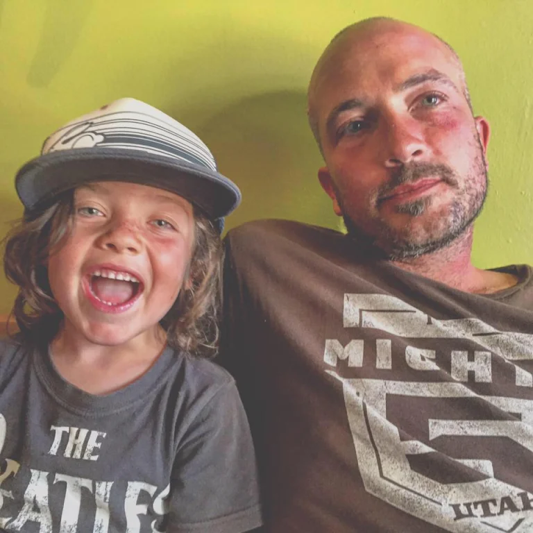 Nathan Swartz, Durango resident since 2018 and web developer, sits smiling with one of his children who is having a blast and laughing