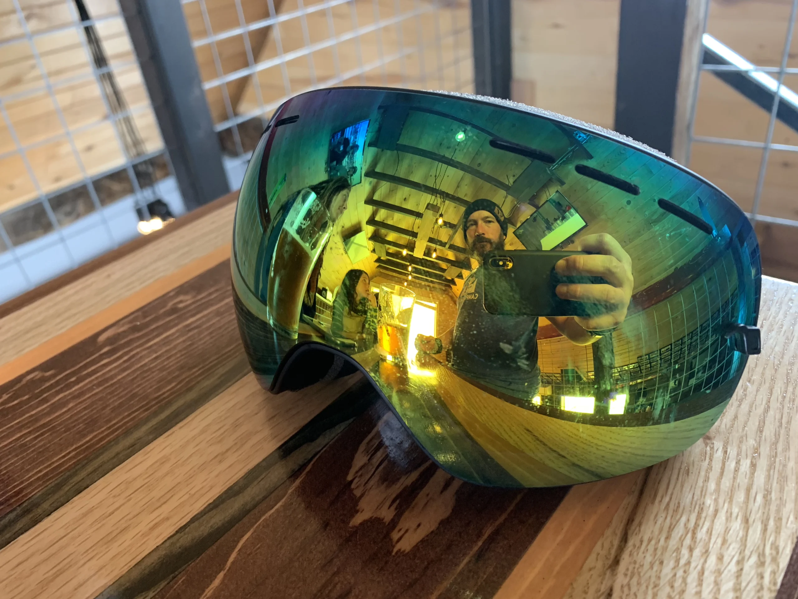 a man and his son enjoying beverages in the loft of a cabin, the Nugget Mountain Bar, as seen reflected in a pair of snowboard goggles